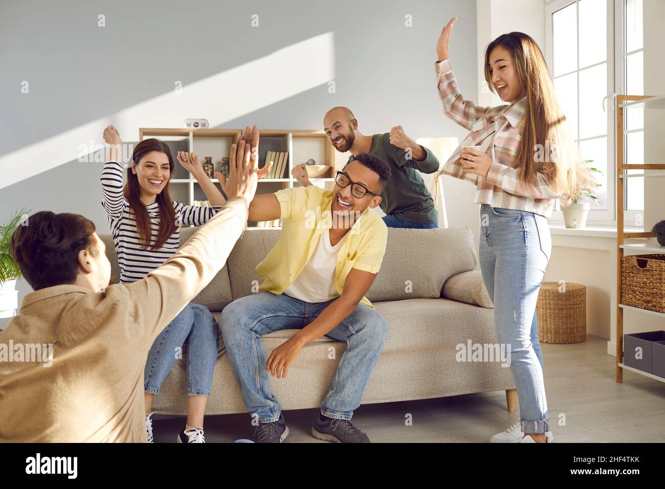 Two cheerful multiracial men give high five to each other while having fun at home with friends. Stock Photo