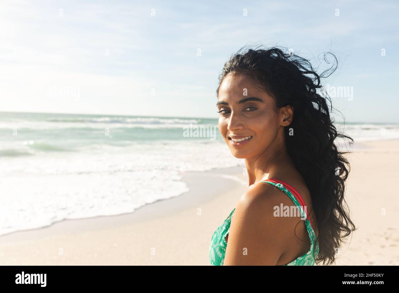 Portrait of smiling beautiful young biracial woman looking over shoulder at beach enjoying sunny day Stock Photo