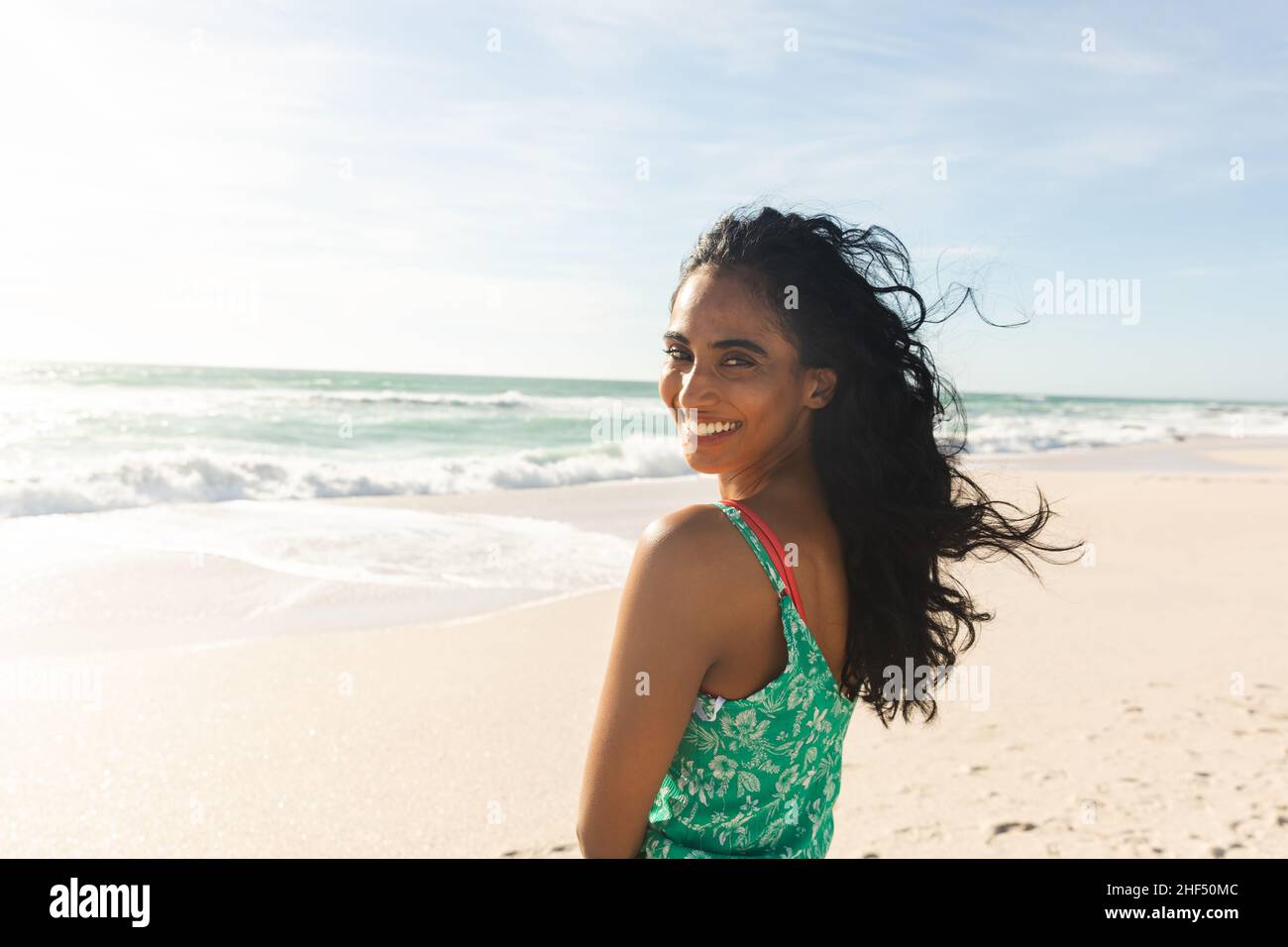 Portrait of happy beautiful young biracial woman looking over shoulder at beach enjoying sunny day Stock Photo
