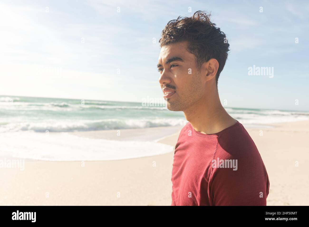 Biracial man looking away while standing at beach against sky on sunny day Stock Photo