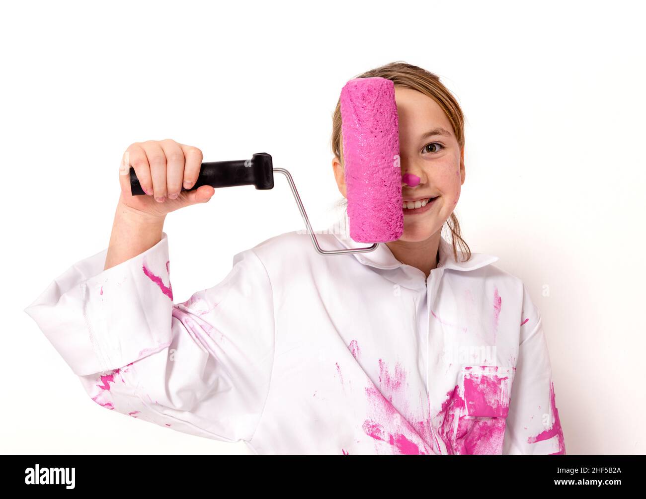 Young girl, 10 years old, holding a roller with pink paint in front of her face. She is looking at the camera with a friendly smile. Stock Photo