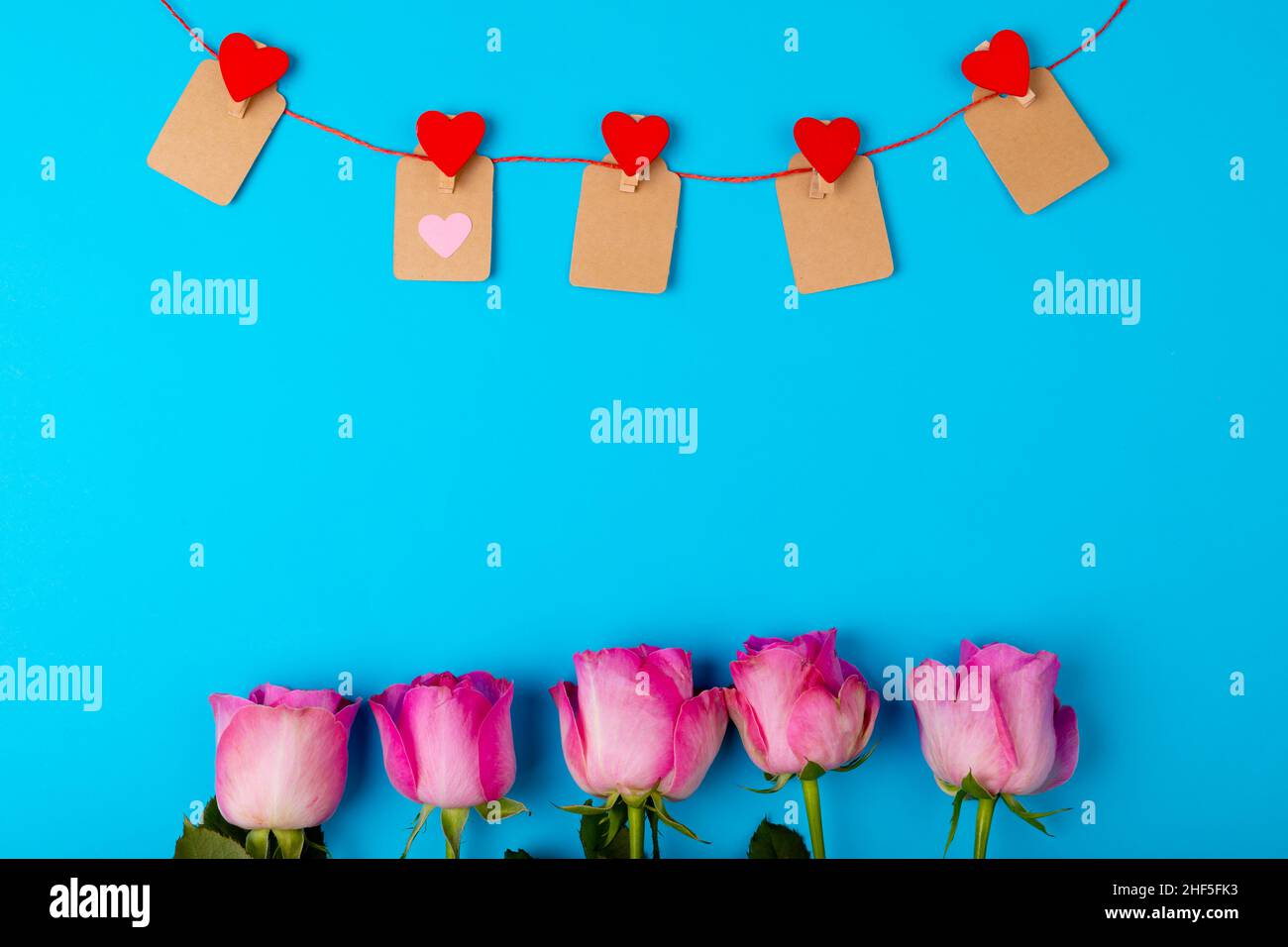 Overhead view of fresh pink roses and heart shaped decoration on blue background, copy space Stock Photo