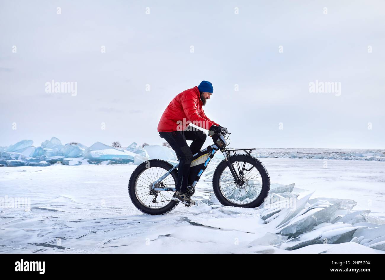 Man with beard in red jacket ride fat bike at frozen ice lake with snow in Kazakhstan Central Asia Stock Photo