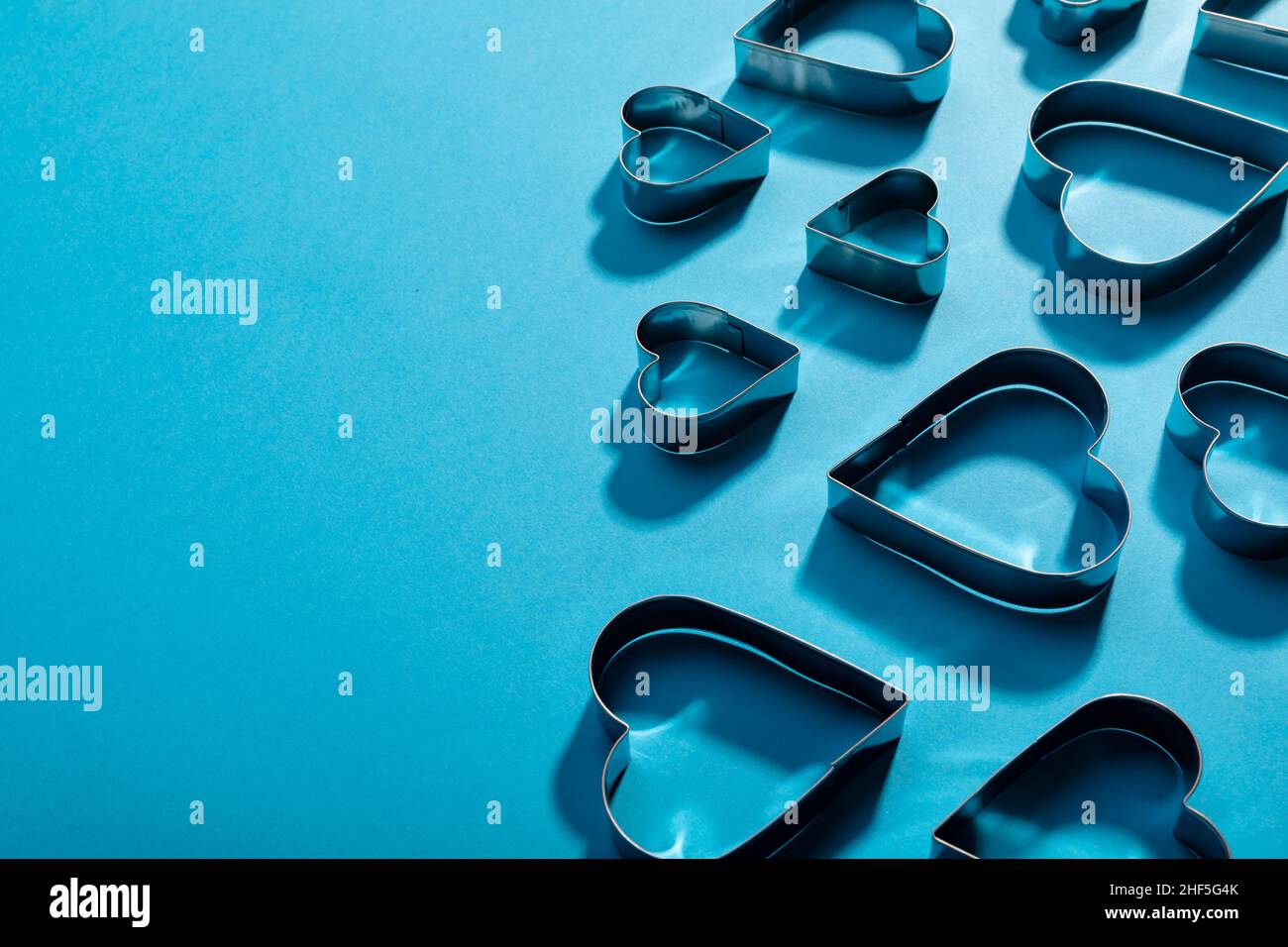 High angle view of heart shape pastry cutters with shadows by copy space on blue background Stock Photo