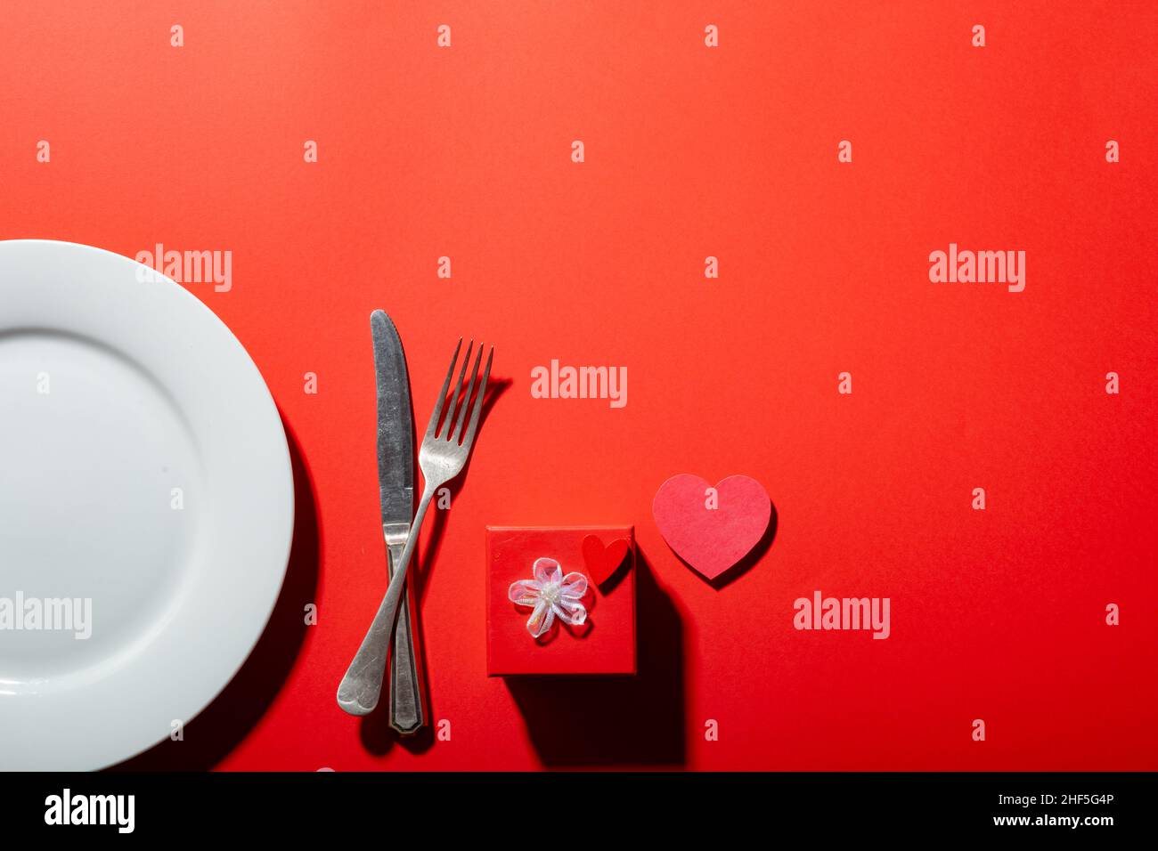 Empty plate with cutlery by heart shape and valentine present box on red background with copy space Stock Photo