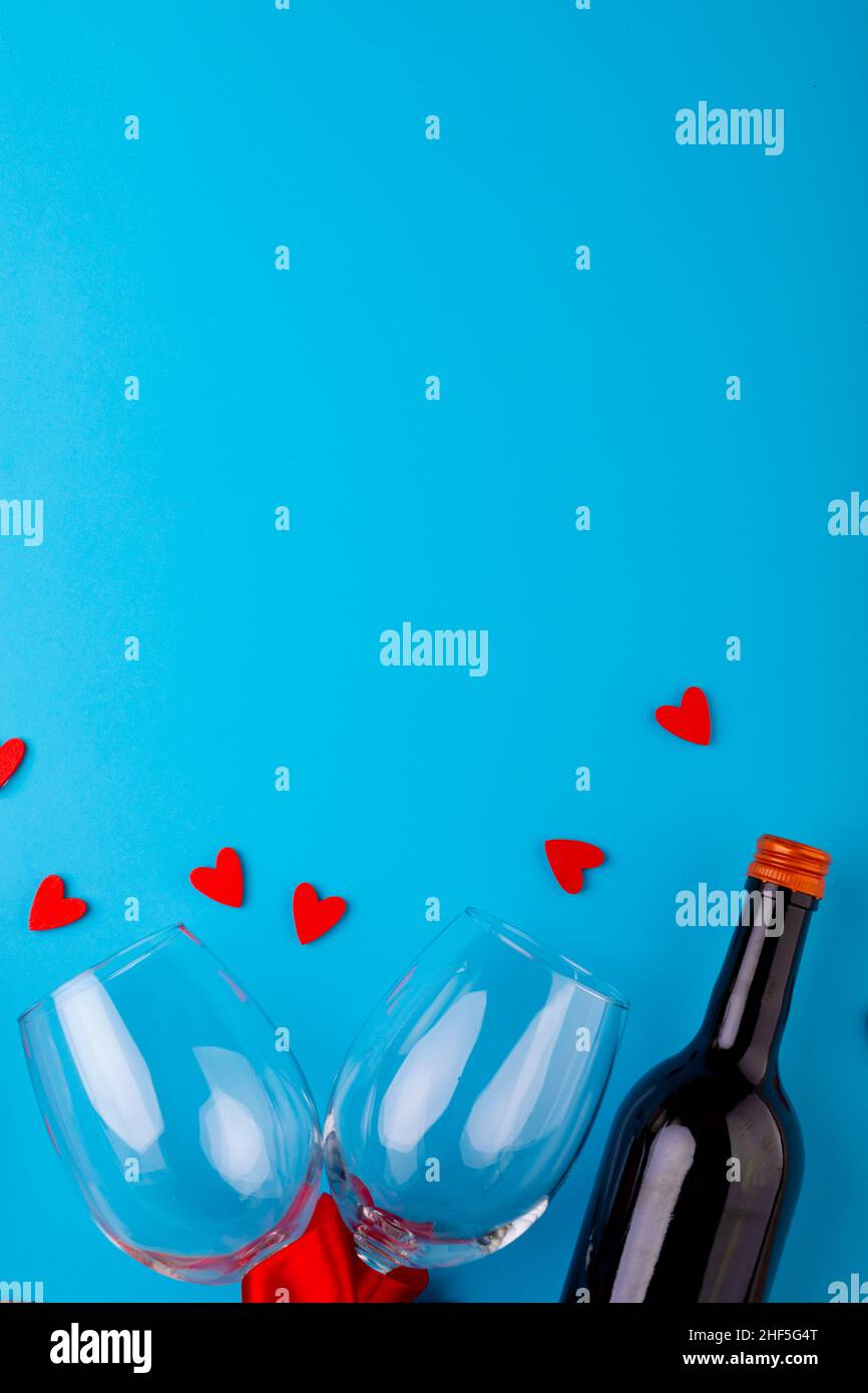 Red heart shapes by wine bottle and empty wineglasses over blue