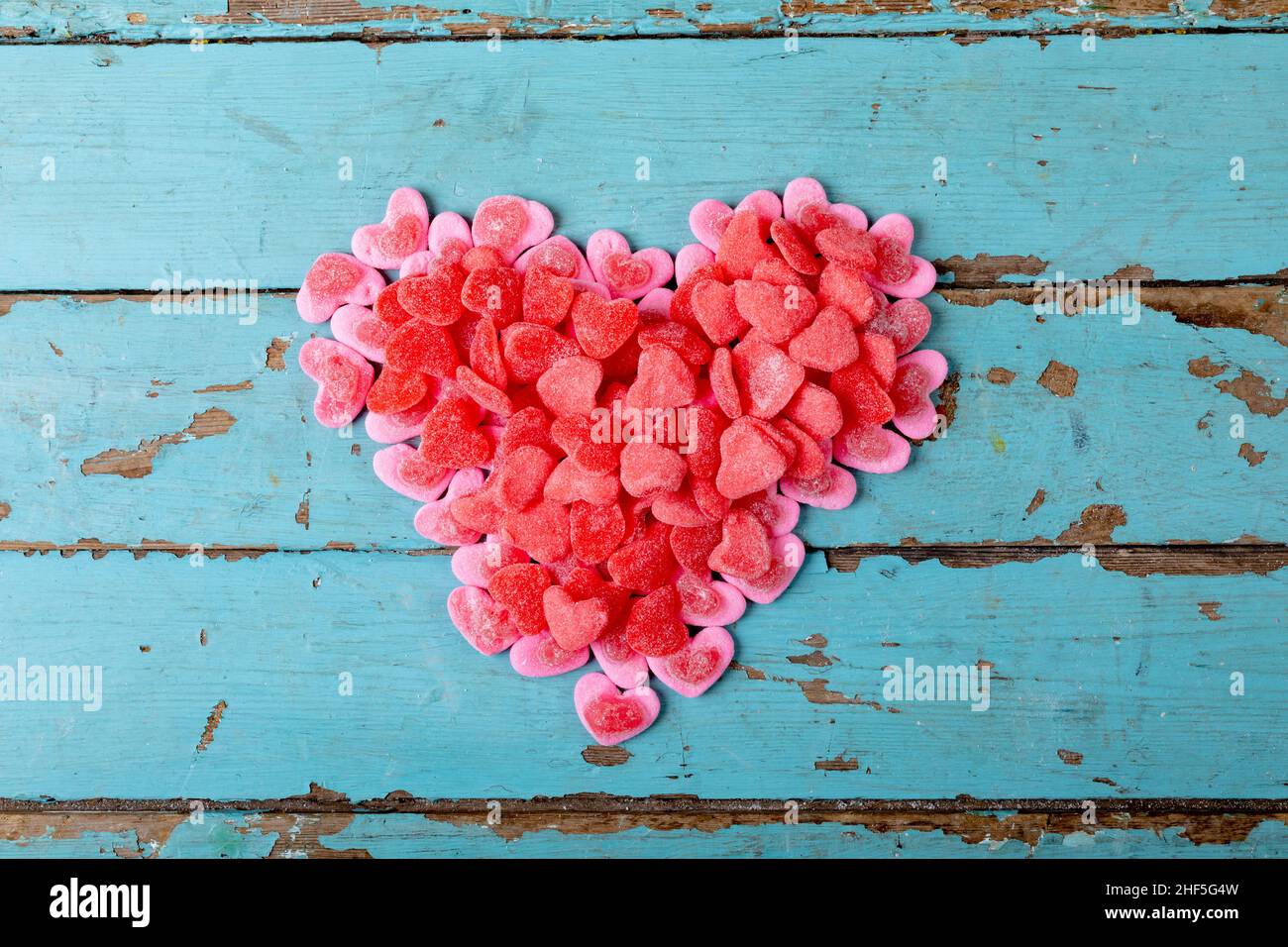 Overhead view of sweet pink and red candies making heart shape on blue wooden table with copy space Stock Photo