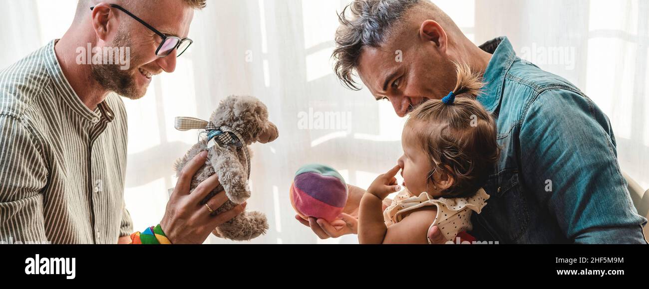 Horizontal banner or header with male gay couple with adopted baby girl at home - Two fathers playing with their daughter - Lgbtq+ family at home - Di Stock Photo