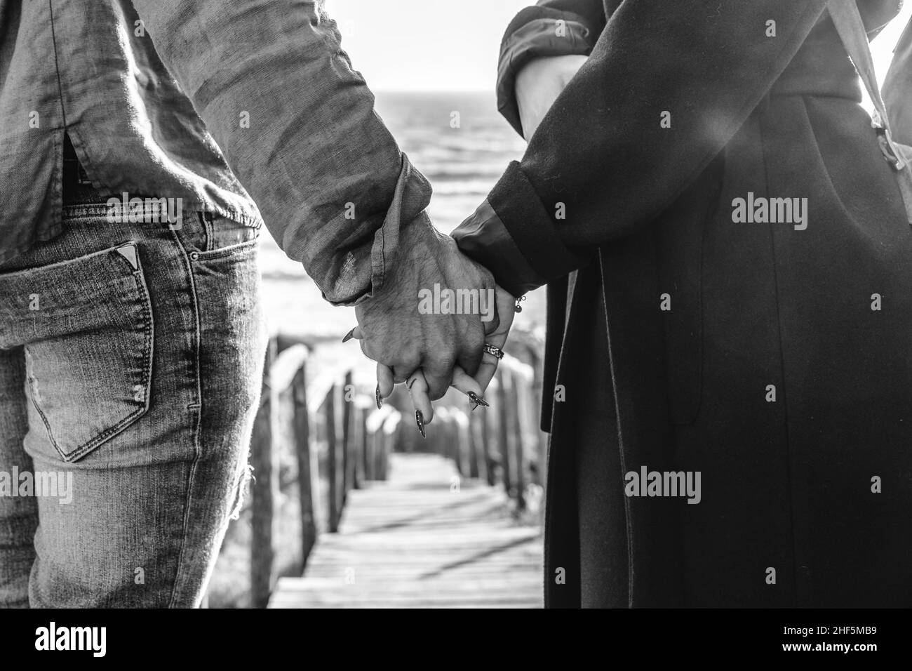 Closeup of young couple holding hands walking down on wooden stair towards the beach - Hipster couple, holding hands, in love enjoying romantic evenin Stock Photo