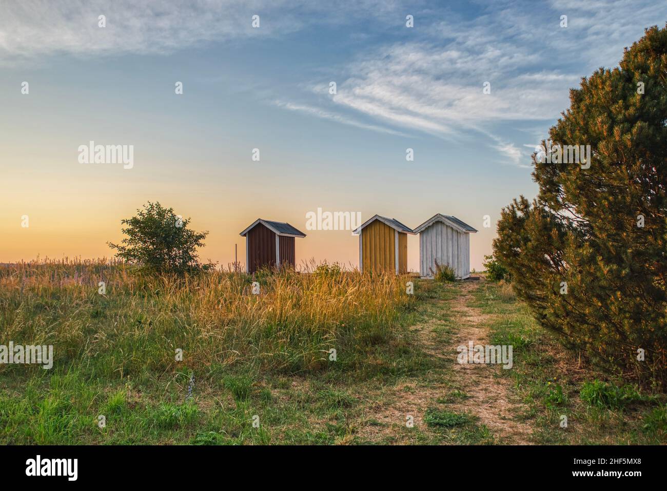 Three rustic summerhouses at sunset on a strand show nordic summer vacation. Scandinavian holiday houses illustration conveys a comfort zone concept Stock Photo