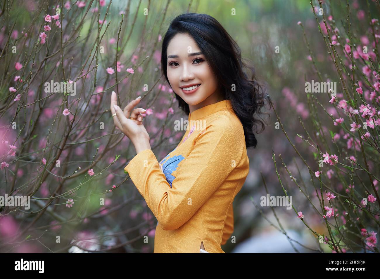 Ho Chi Minh City, Vietnam: Vietnamese girl wearing ao dai posing with peach blossoms to celebrate the new year Stock Photo