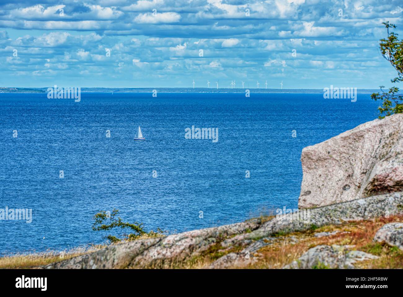 Faraway, small sailing boat or sailboat travelling solo at sea by the Isle of Hano, Sweden conveys peace or tranquility on a lone summer vacation Stock Photo