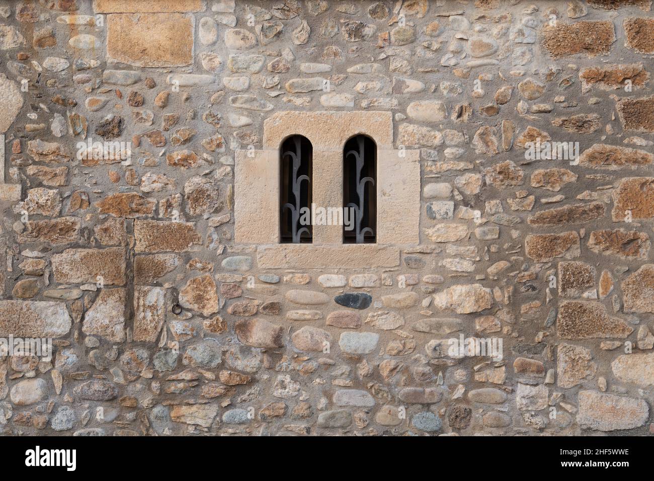 Old stone wall with a double arched window and metal grating Stock Photo