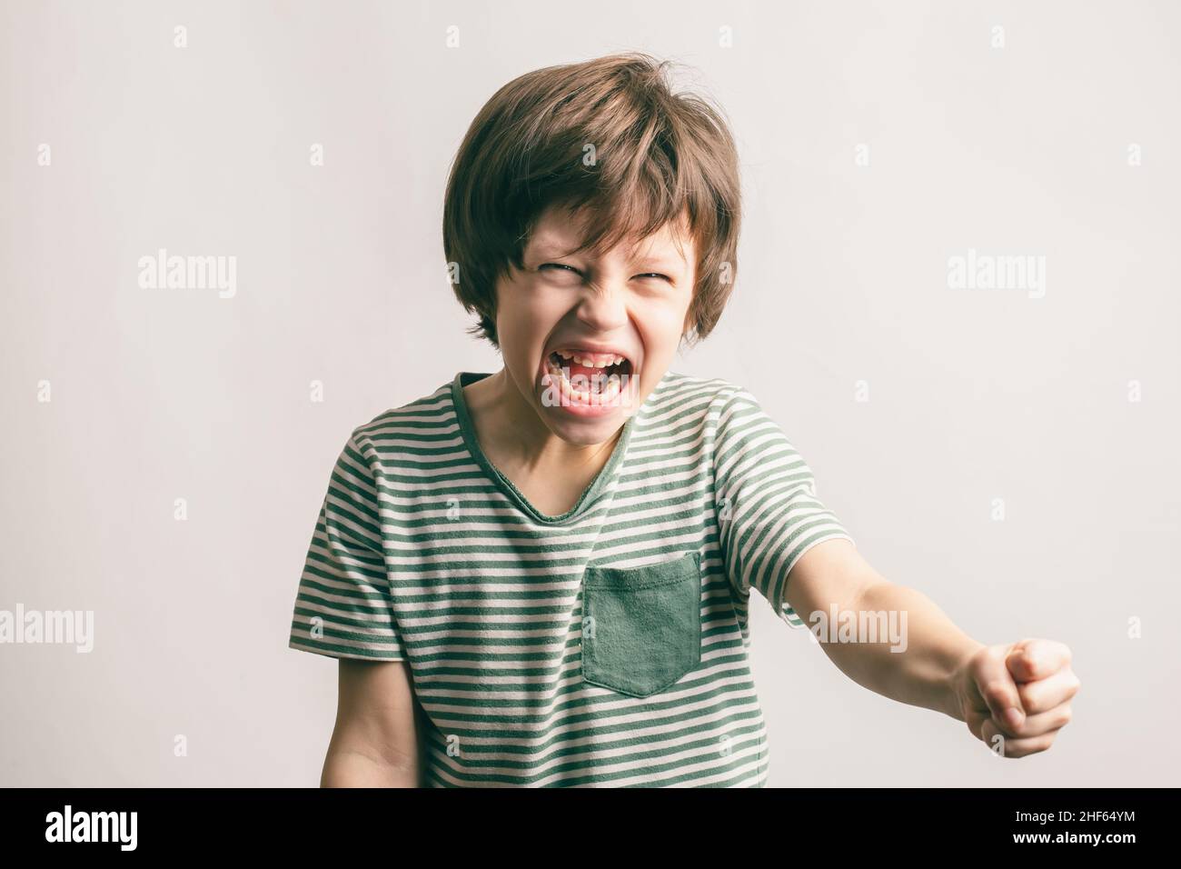 Angry kid shouting and rising his fist. Aggressive little boy with mouth wide open looking to the camera. ADHD syndrome Stock Photo