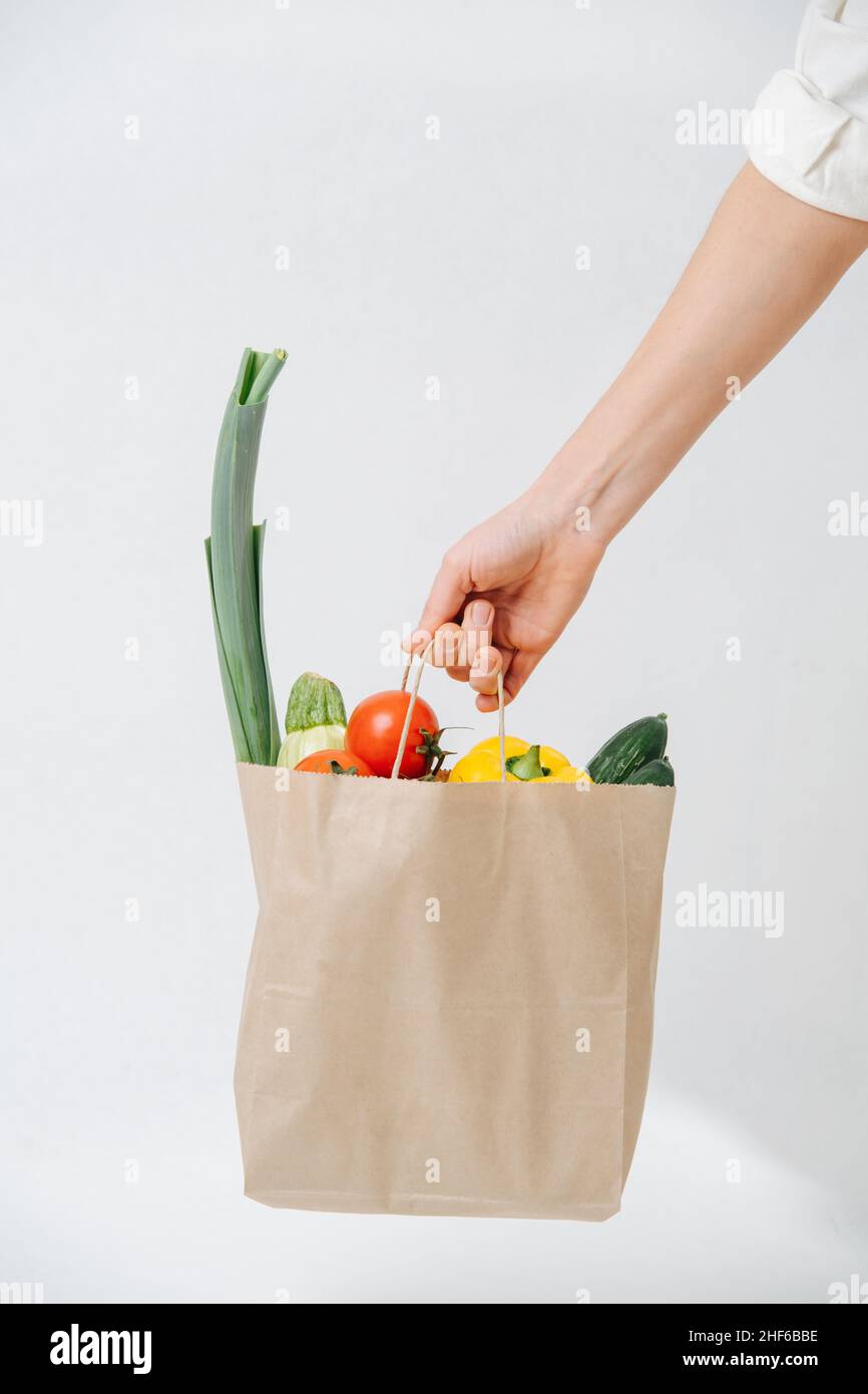Hand holding grocery paper bag filled with colorful vegetables over white background. Eco friendly compostable products. Stock Photo