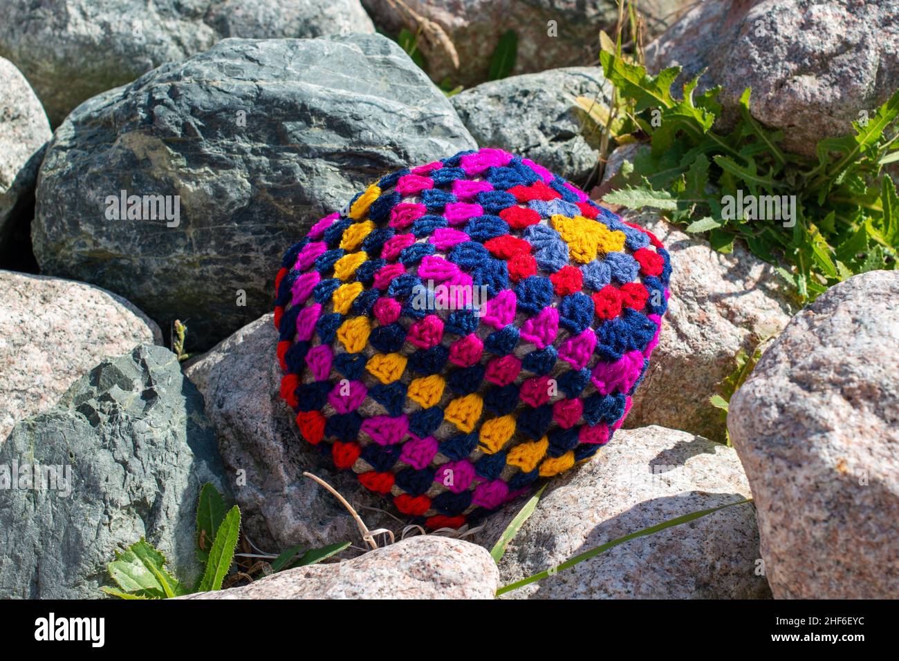 A colorful craft crocheted pillow, multicolored; red, purple, blue, and yellow color cotton wool. The textile pattern in the handmade pillow is a flow Stock Photo