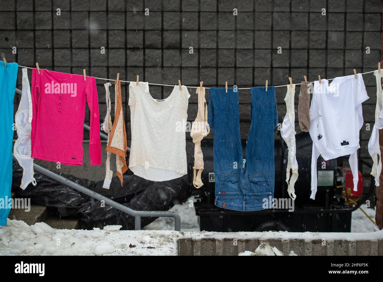 A clothesline of dark and red clothes hangs on a line with two ground sticks and lots of clothespins. The natural way of drying clothes outdoors. Stock Photo