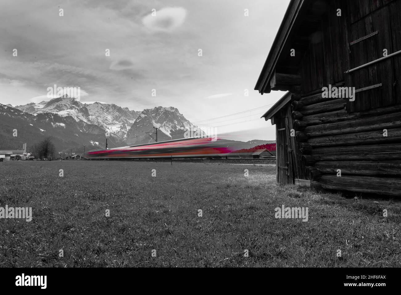 A red Deutsche Bahn train travels to Garmisch-Partenkirchen,  through the fields,  past a tree stump,  Bavaria,  Germany Stock Photo