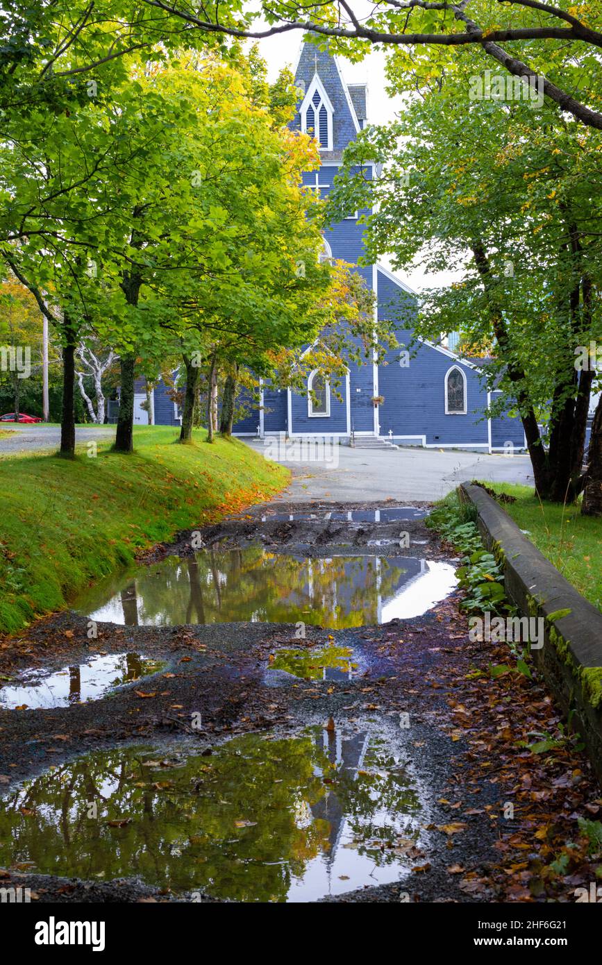 An old royal blue wooden church with white trim nestled among vibrant green and yellow colored trees. There's a long driveway leading to the building Stock Photo