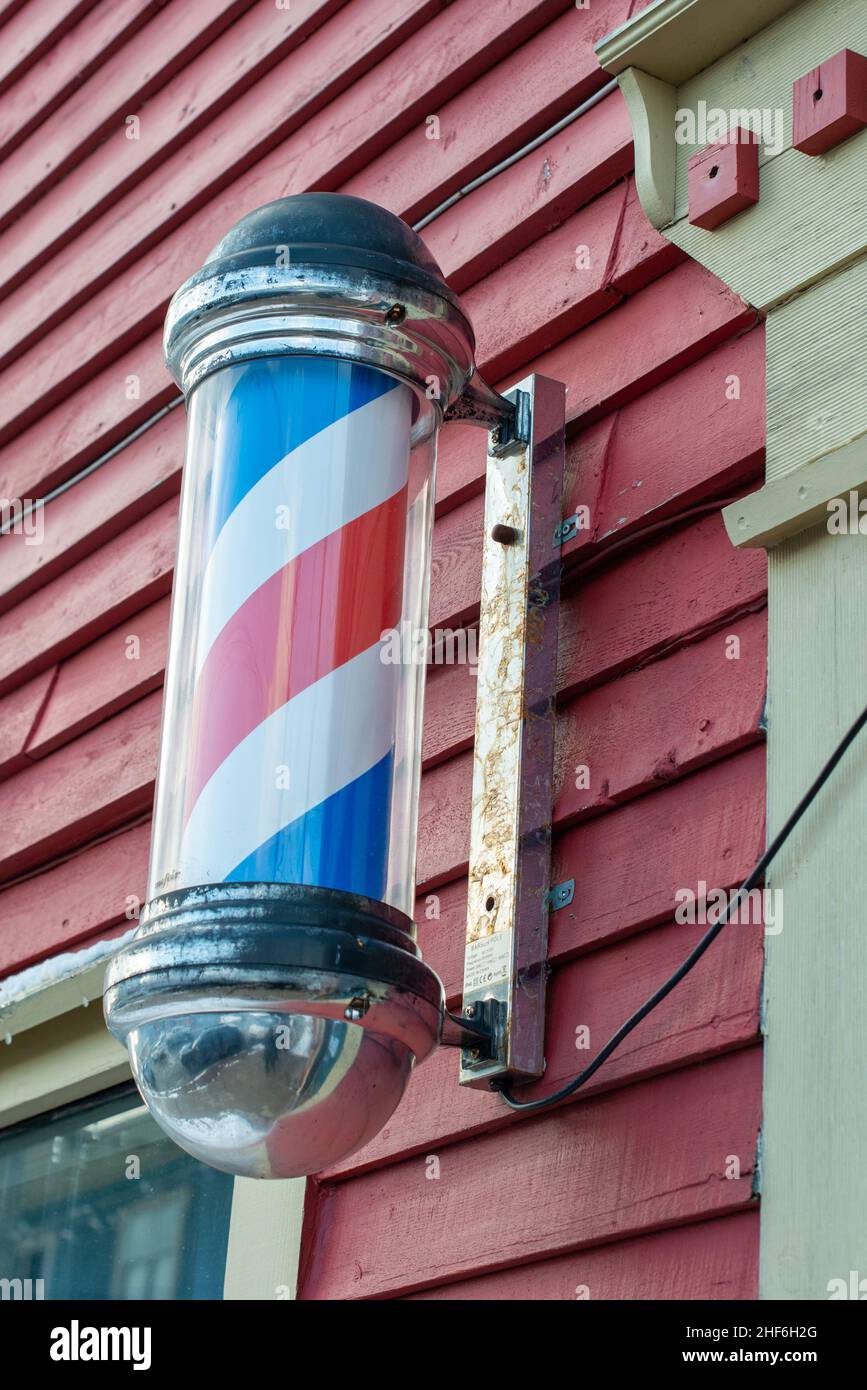 Barbershop pole with red, blue, and white stripes moving around on the outside of a barbershop. The vintage nostalgic pole is attached to a wall. Stock Photo