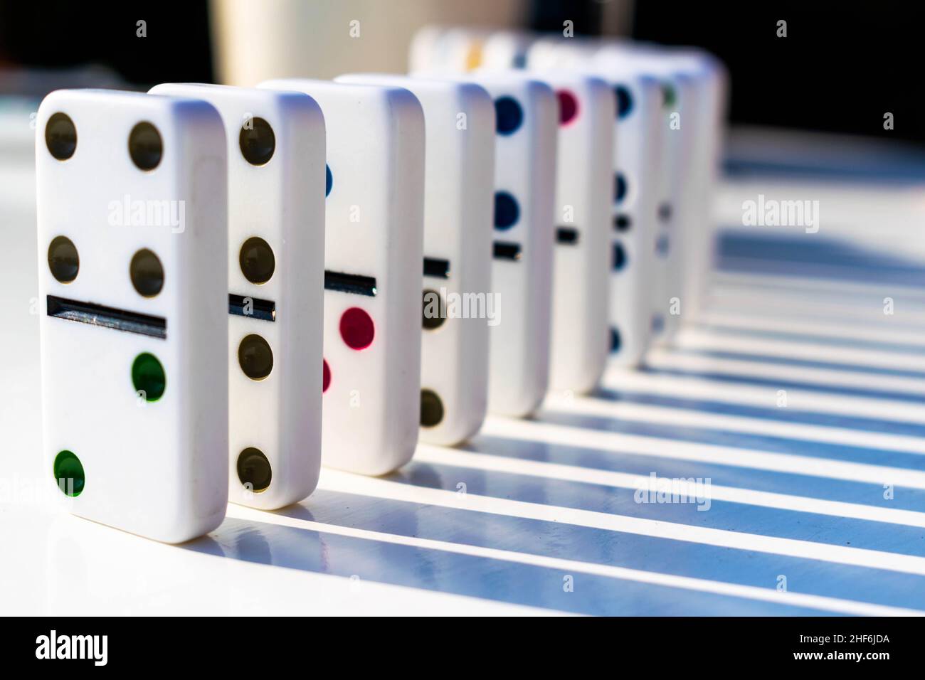 White domino tiles standing neatly on a white table ready to be pushed or fall over. Concept for family fun and dominoes games, organisation, OTC Stock Photo