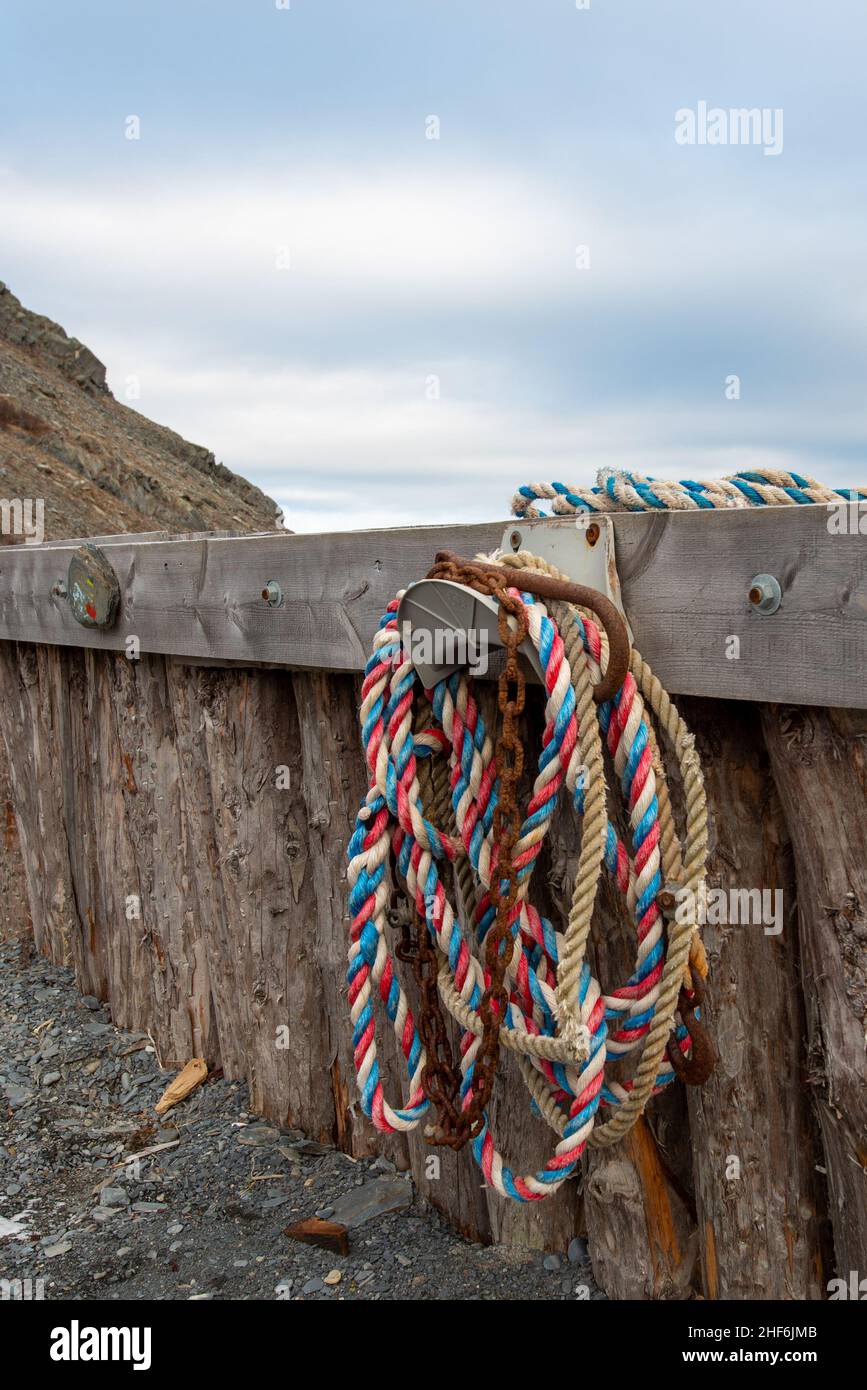 Multiple red, blue, and white braided nylon fishing ropes hanging from a metal hook on a wooden wharf with a blue cloudy sky background. Stock Photo