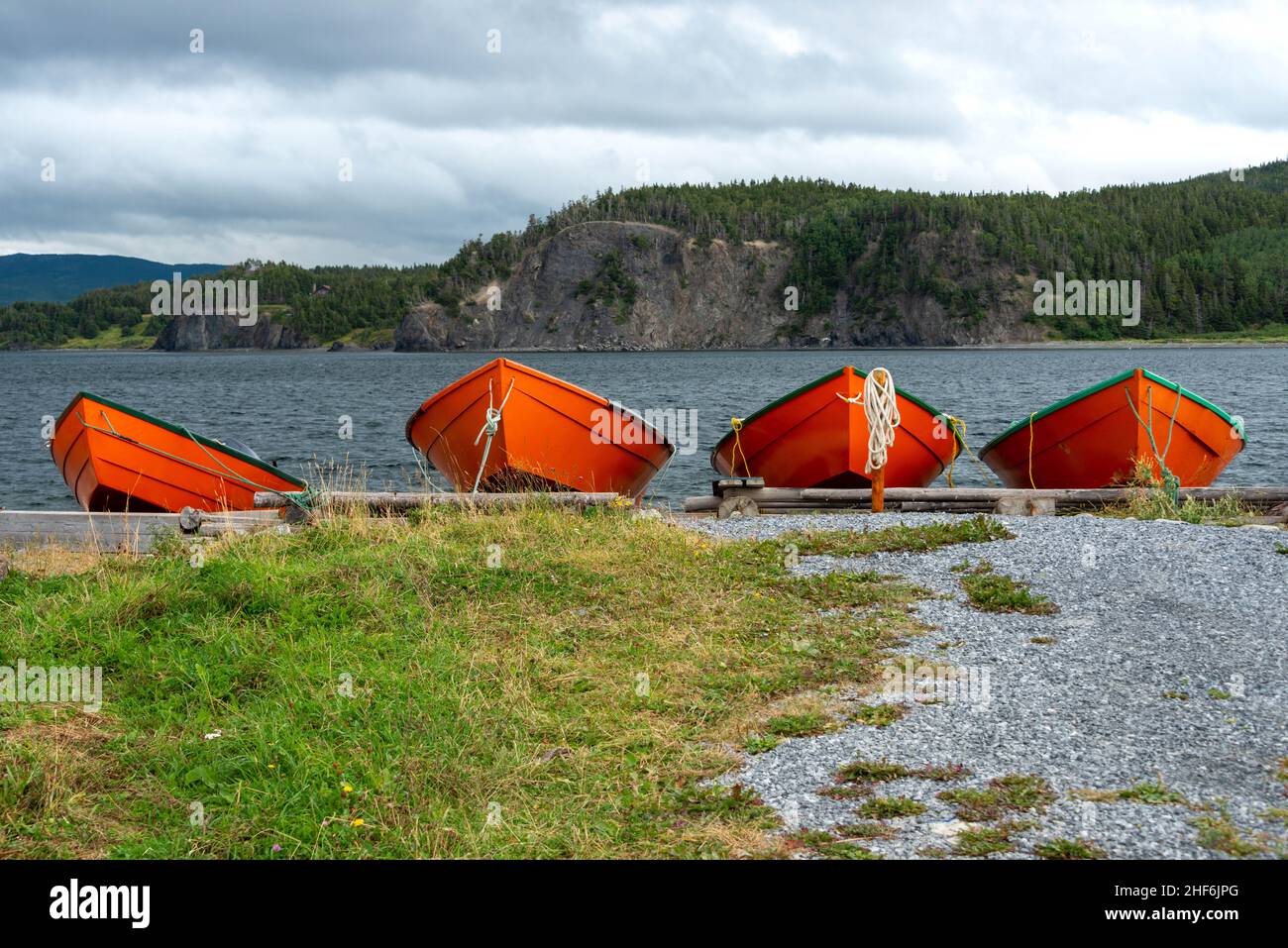 Bright, colorful, orange and green wooden traditional style fishing vessels, wood boats, on a beach. There are mountains, rocky coastlines, lush green Stock Photo