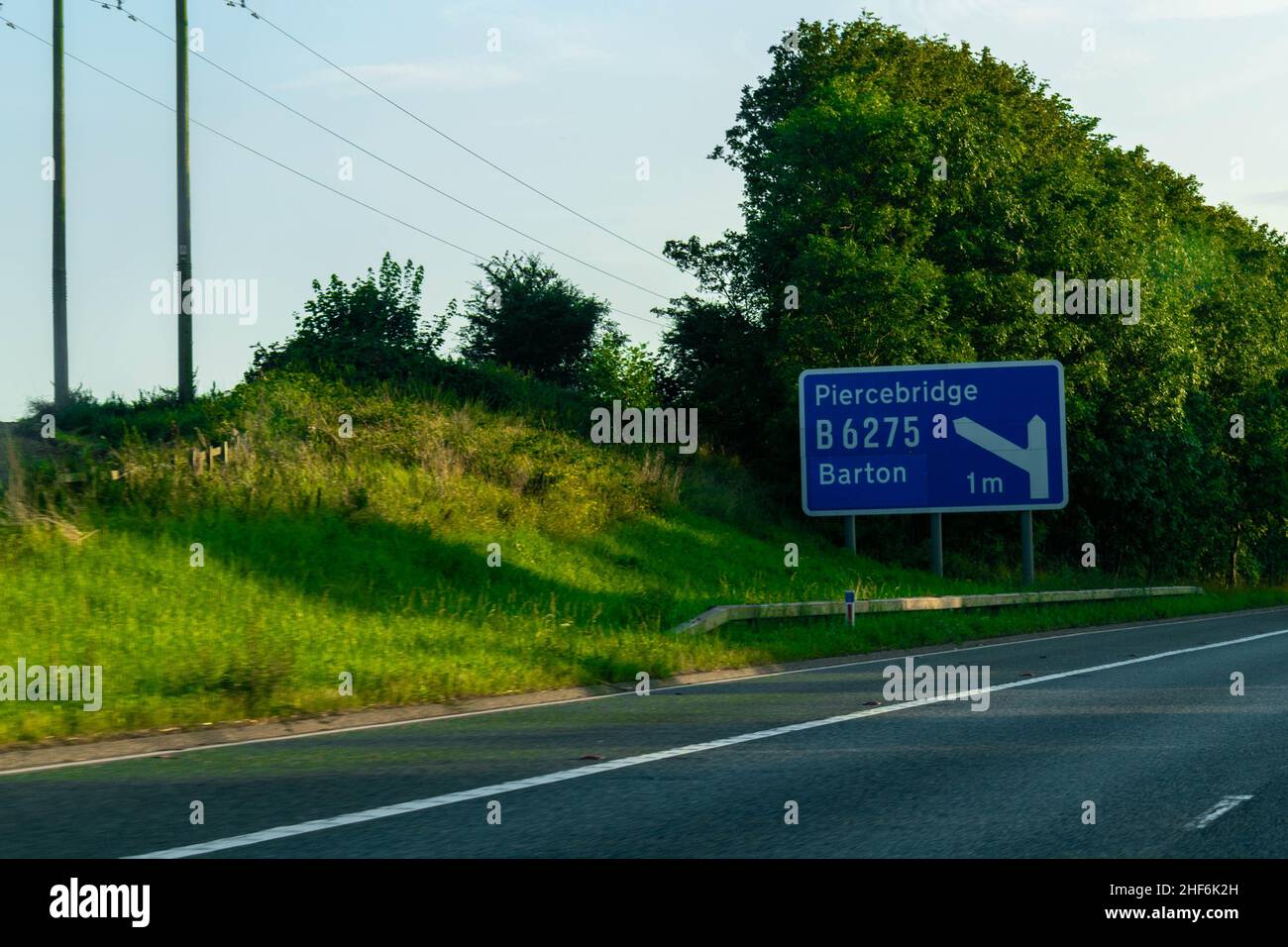 Blue British Motorway sign with space for copy text on the A1 motorway directing traffic drivers towards Piercebridge and Barton, B6265. Junction. Tra Stock Photo