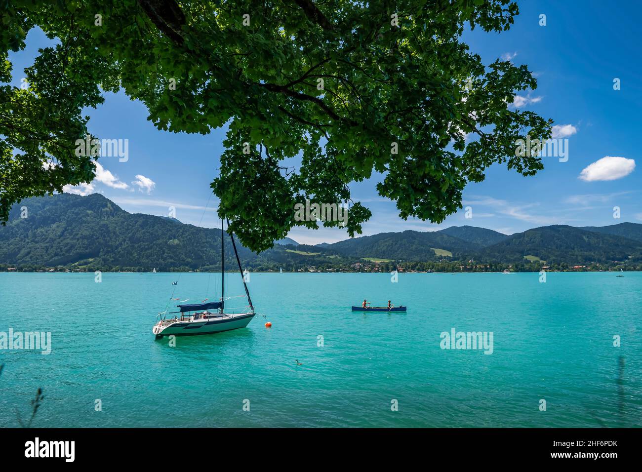 Turquiose Tegernsee. The popular lake in the heart of bavaria with a beautiful green bluish water color in summer with a boat and two canoying people Stock Photo
