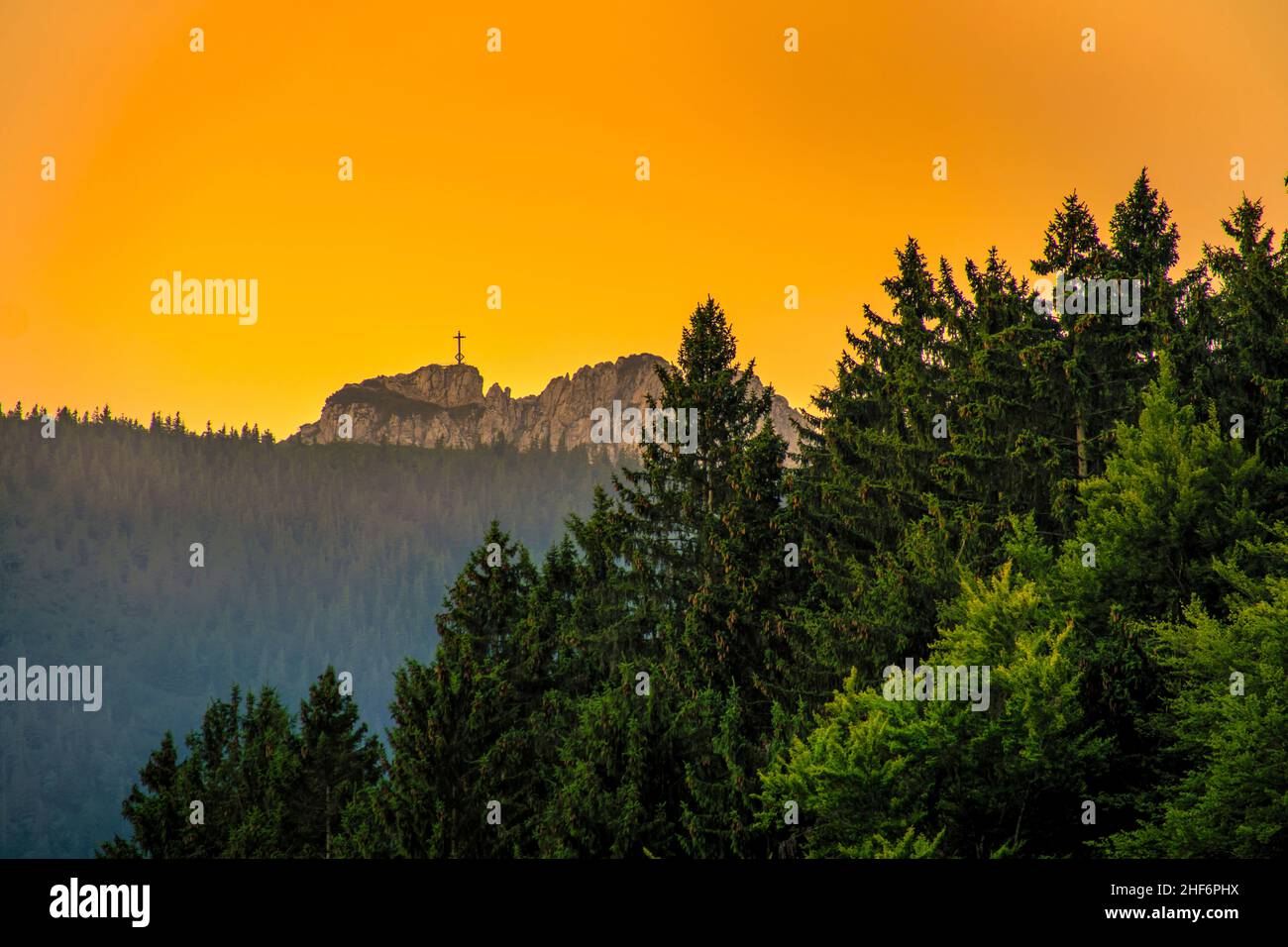 View at the Kampenwand cross at a wonderful golden hour light from far away at the peak of the alpine mountain peak. Stock Photo