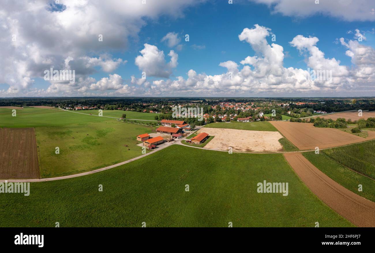 Aerial view over a ranch with horses and a village in the background under a blue,  wonderful fluffy clouded sky Stock Photo