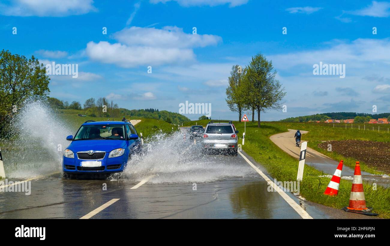 High standing water in germany,  a global threat caused by the global warming. A car splashes the high water away,  driving on a flooded stree Stock Photo