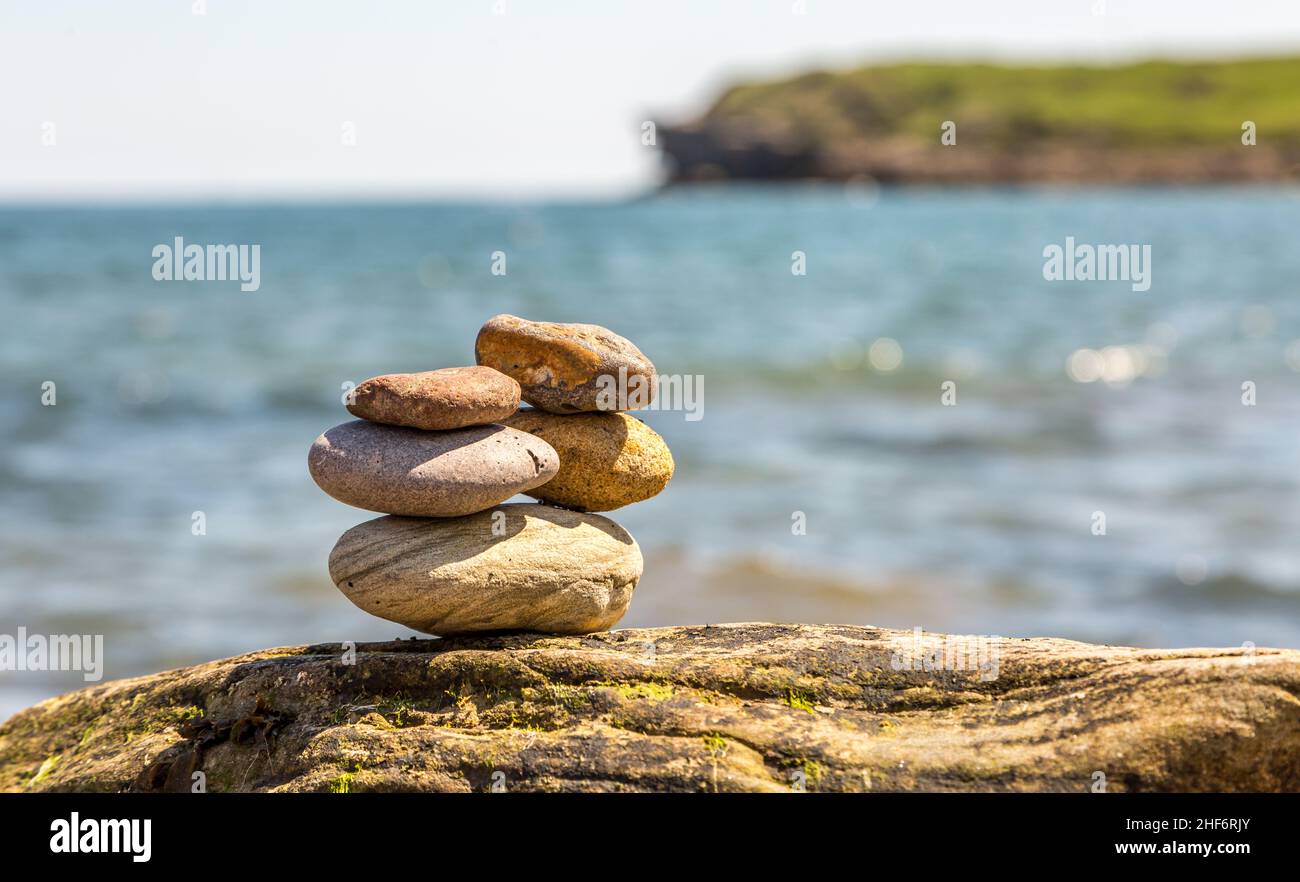A stone cairn balanced on a rock with sea & cliffs in the background Stock Photo