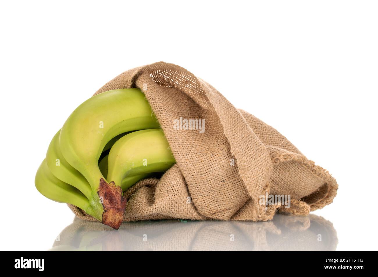 One bunch of organic green bananas in a jute bag, closeup, isolated on