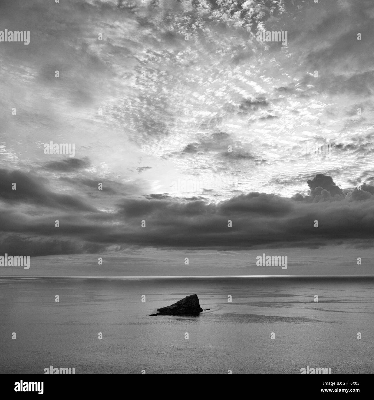 A rock juts out of the sea at sunset Stock Photo