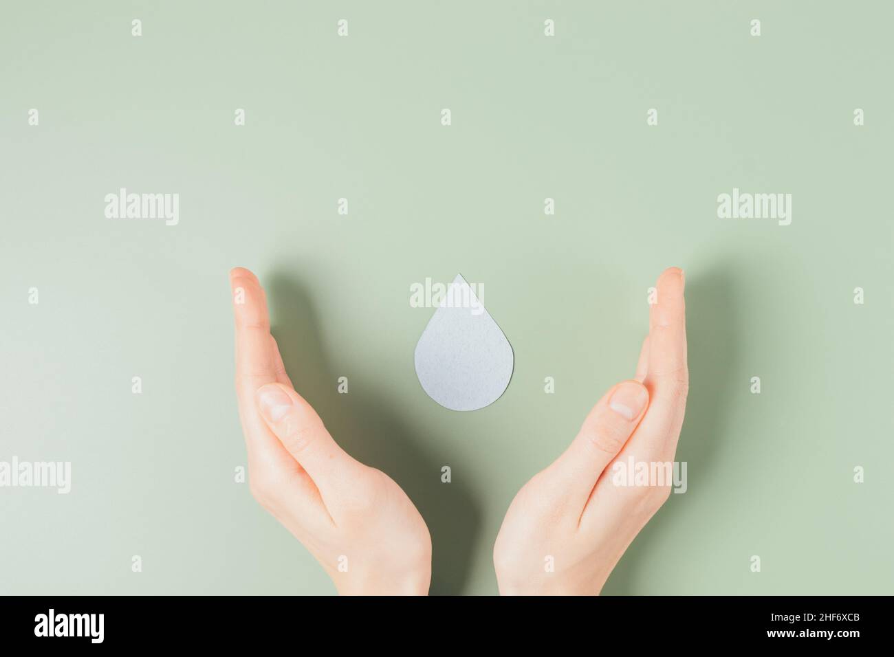 Save water concept, female hands carefully hold drop of water on green background, flat lay Stock Photo