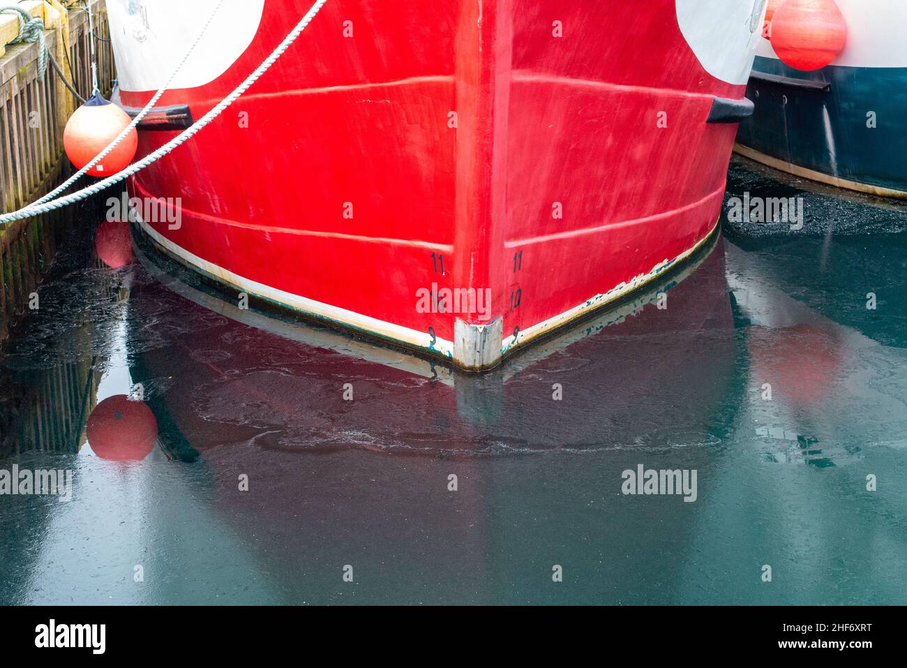 A vibrant red metal ship with black and white waterline measurement markers or load lines on the hull of the vessel. The meter numbers 11,10, and 9. Stock Photo