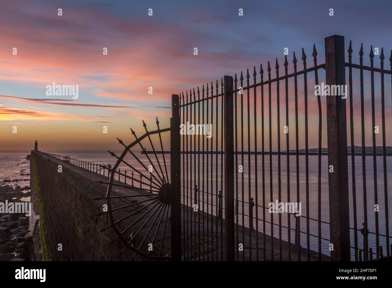 Tynemouth Pier and the Lighthouse through the metal railings with a beautiful vibrant sunrise Stock Photo