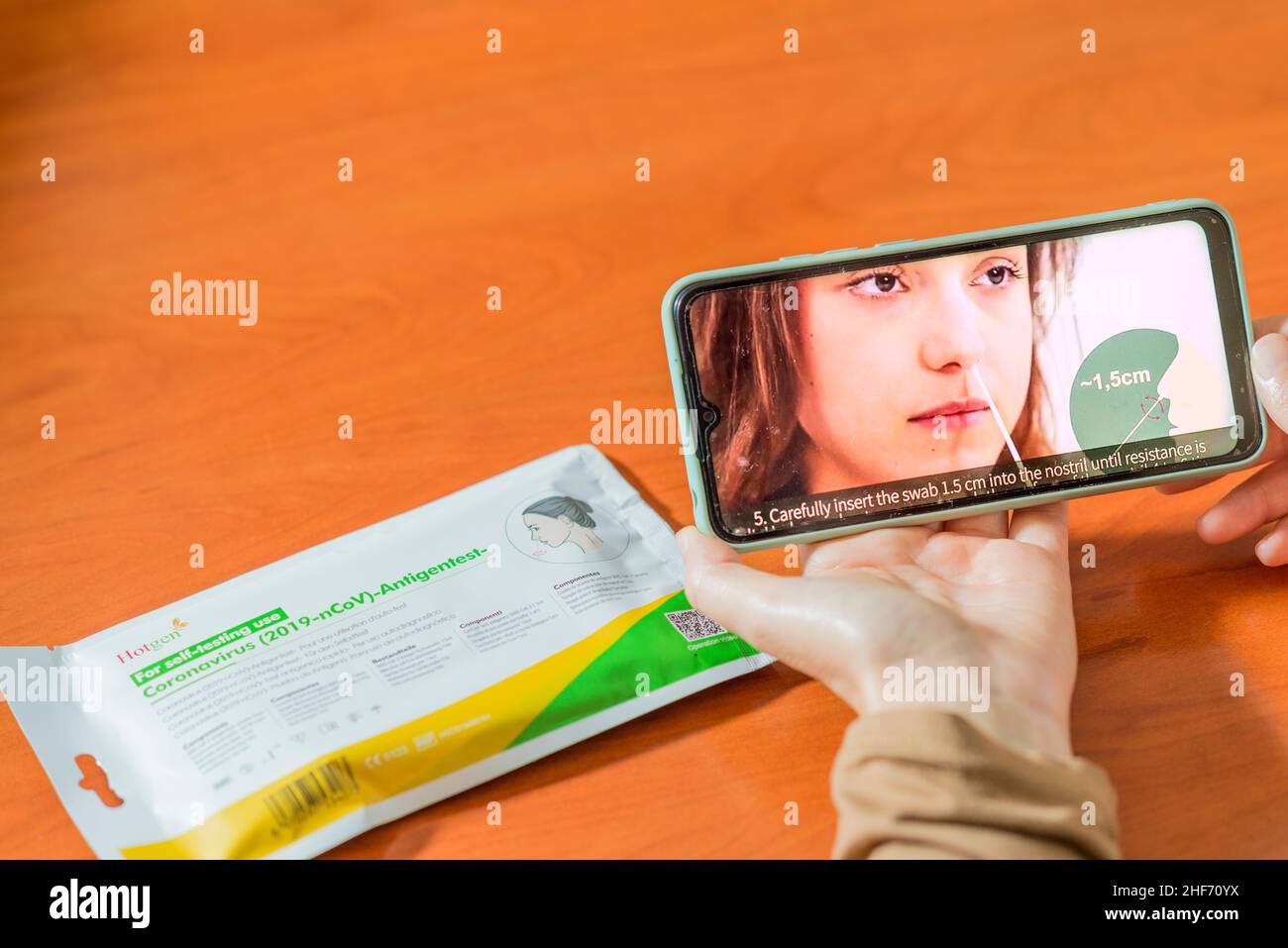 Seville, Spain. 28 December 2021. Detail of a woman's hands holding a smartphone, with a Covid19 self-test kit on a wooden table, watching a video exp Stock Photo