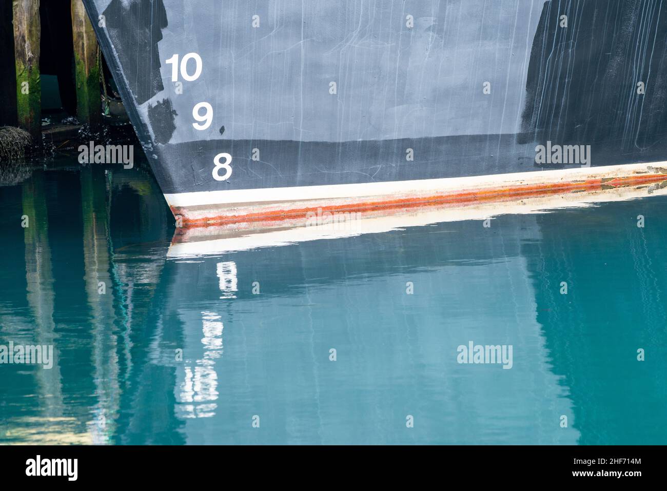 A navy blue ship with waterline marks painted white and red in color. The numbers are painted on the bottom of the boat numbers reflecting in water. Stock Photo