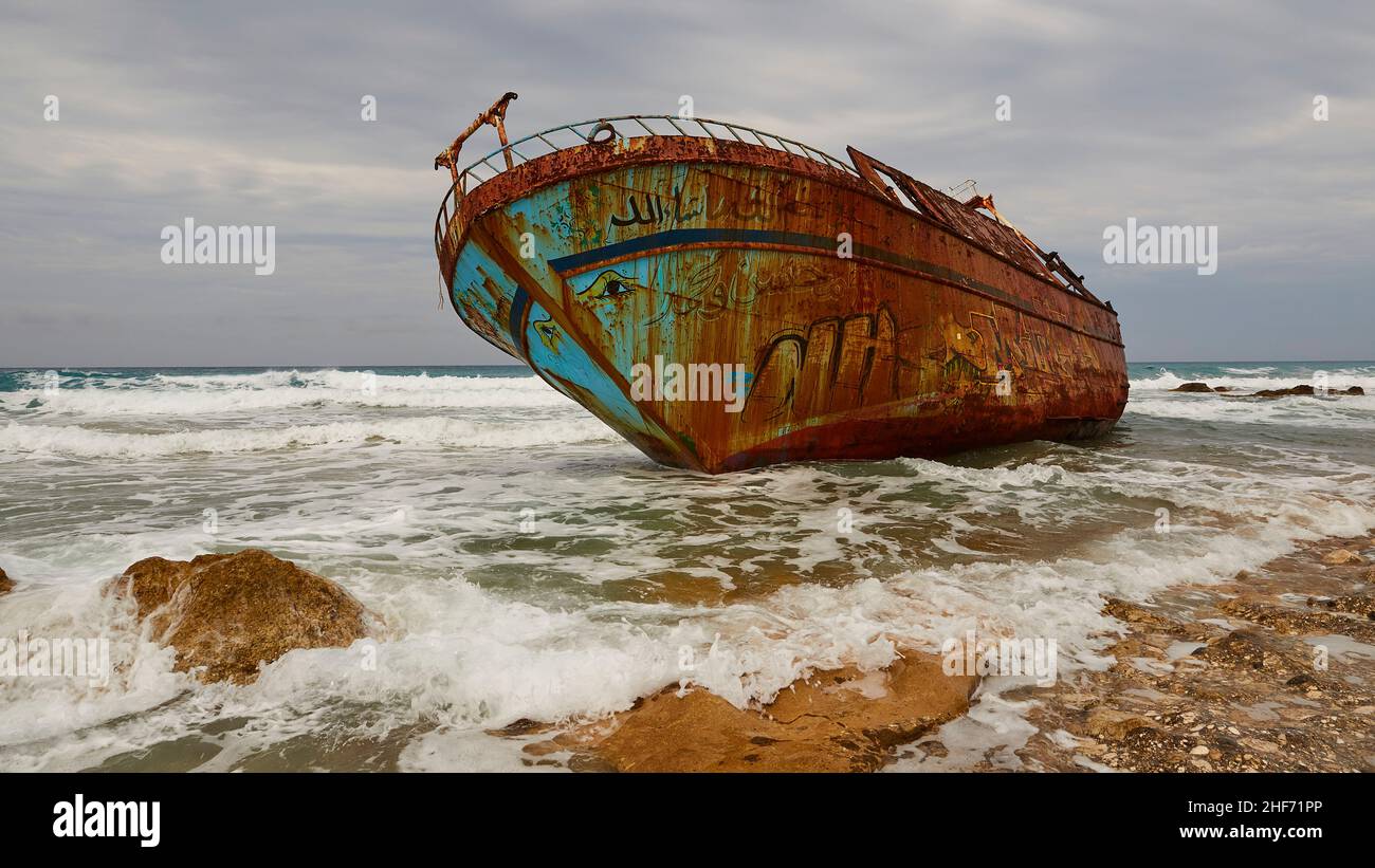 Greece,  Greek Islands,  Ionian Islands,  Corfu,  west coast,  Agios Gordios,  bad weather,  cloudy sky,  shipwreck,  graffiti painting,  surf,  wide-angle view close,  in the foreground rocky coast and searing sea,  wreck from diagonally below,  rusty,  brightly painted Stock Photo