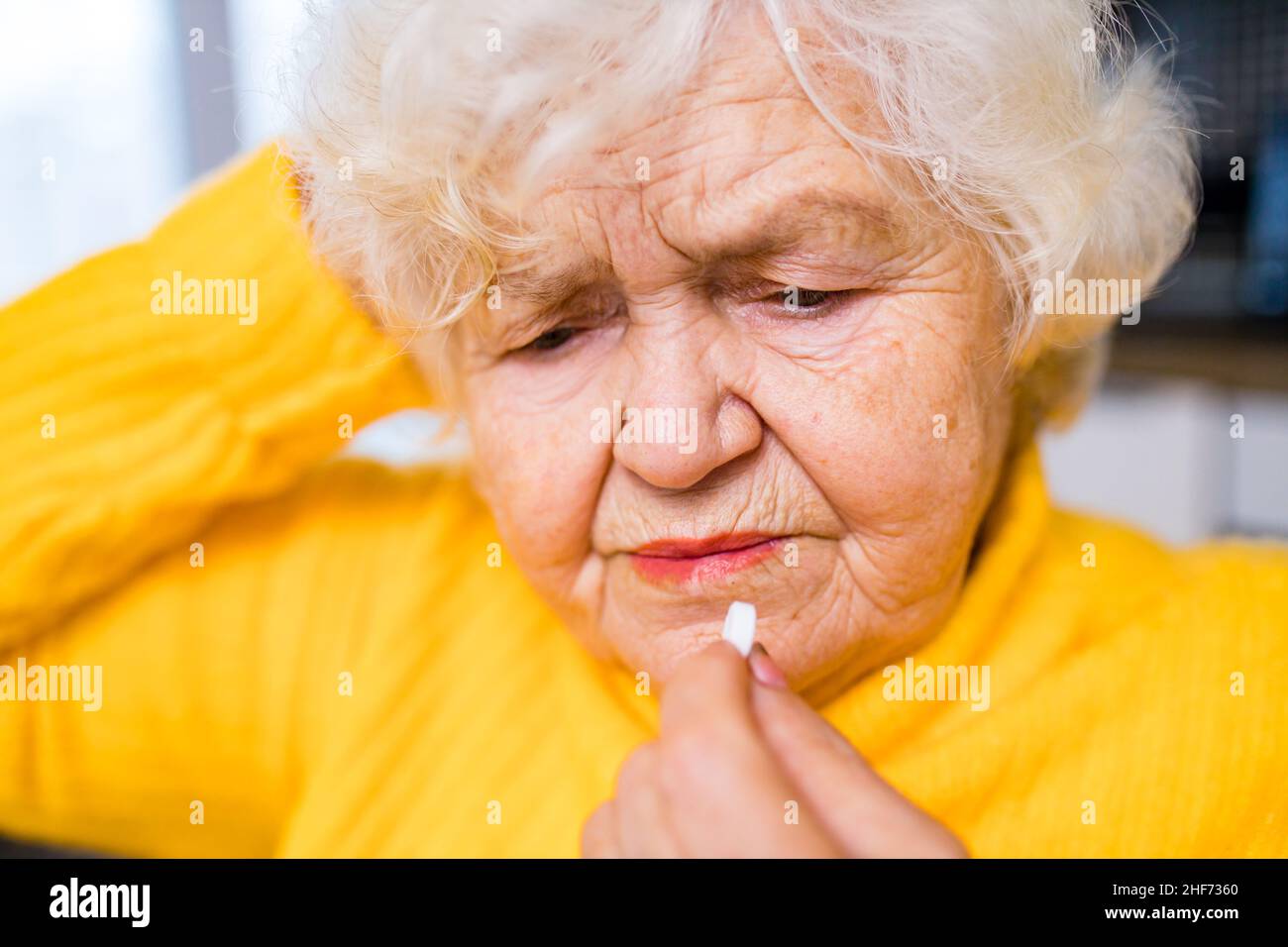 Elderly woman taking pill at home in the kitchen Stock Photo