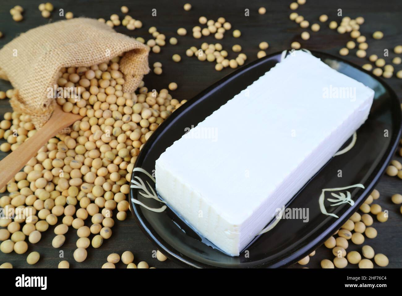 Plate of Soft Tofu Bean Curd with Dried Soybeans Scattered from Burlap Bag in the Backdrop Stock Photo