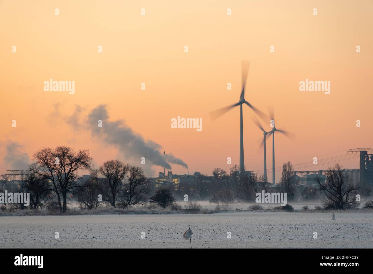 Wind turbines rotate in the Rothensee industrial area in Magdeburg while the setting sun discolors the sky. Stock Photo