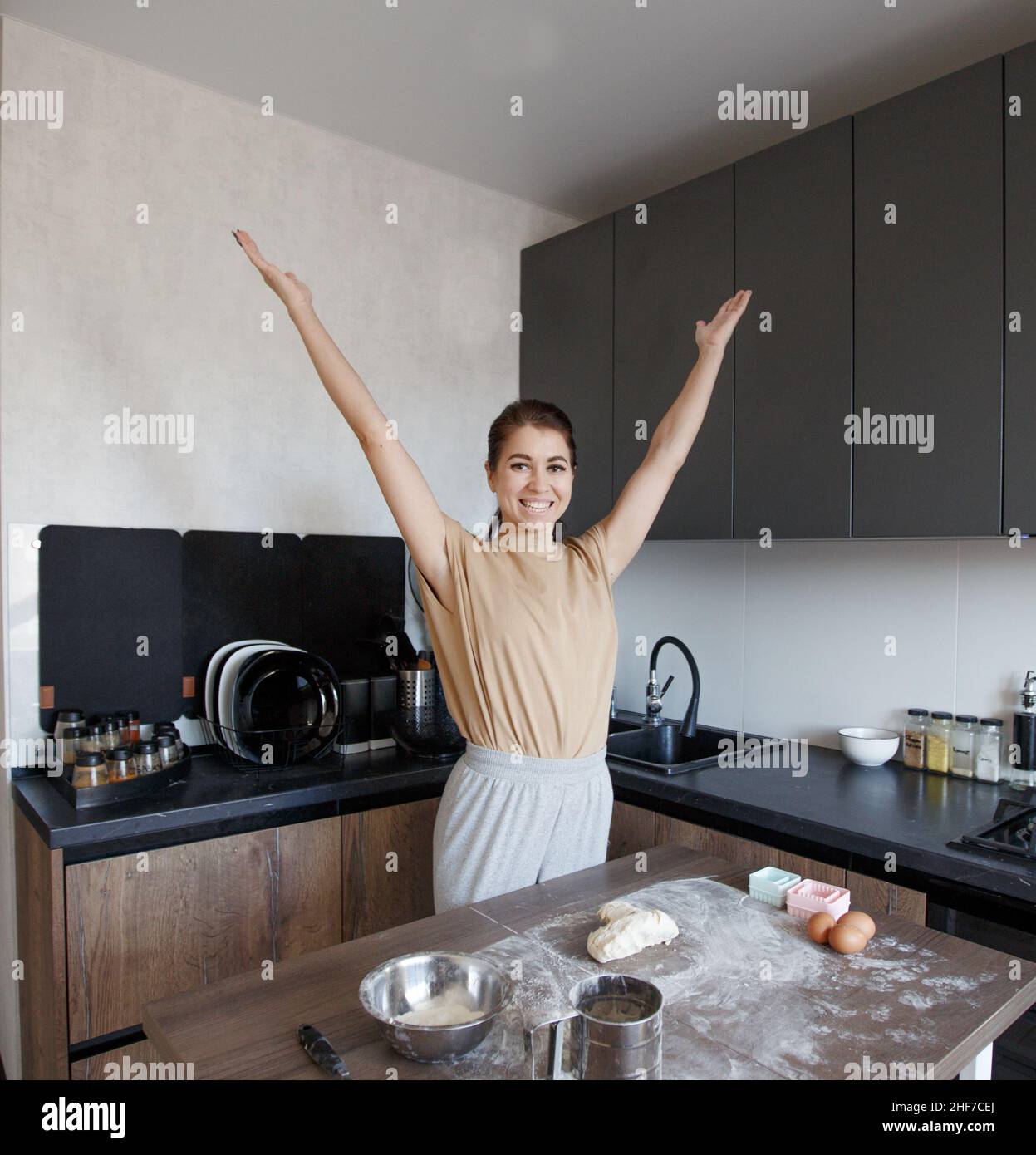 a cheerful girl stands in the kitchen with her hands high up while ...