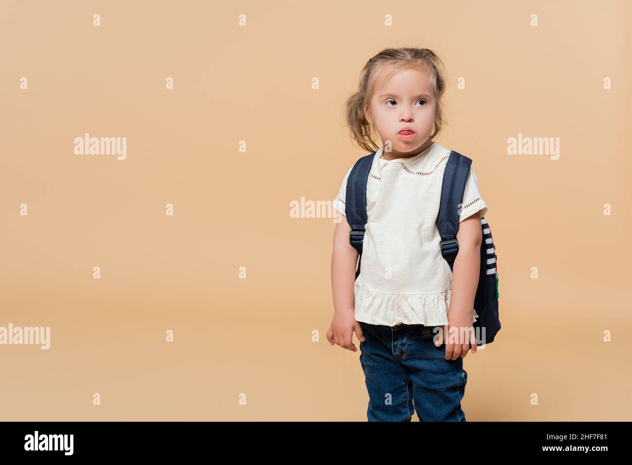 kid with down syndrome sticking out tongue while standing with backpack