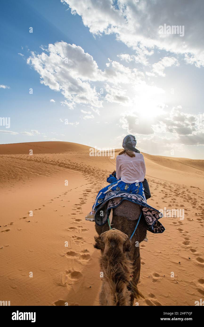 Young girl wearing headscarf riding a dromedary through the erg chebbi