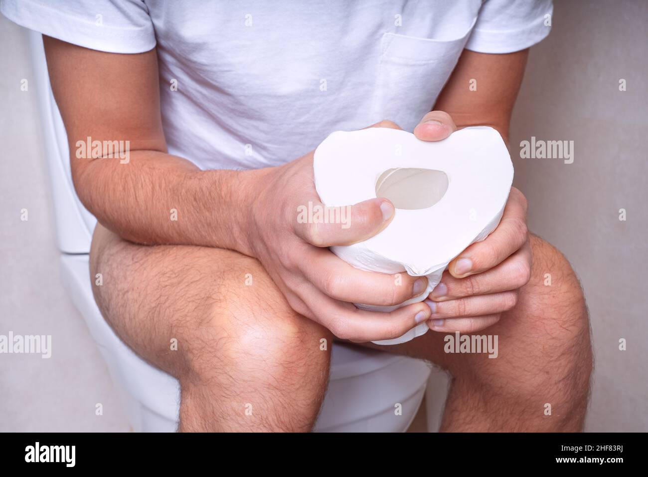 Man sitting on the toilet with toilet paper and suffering from constipation, diarrhea, stomach ache or cramps Stock Photo