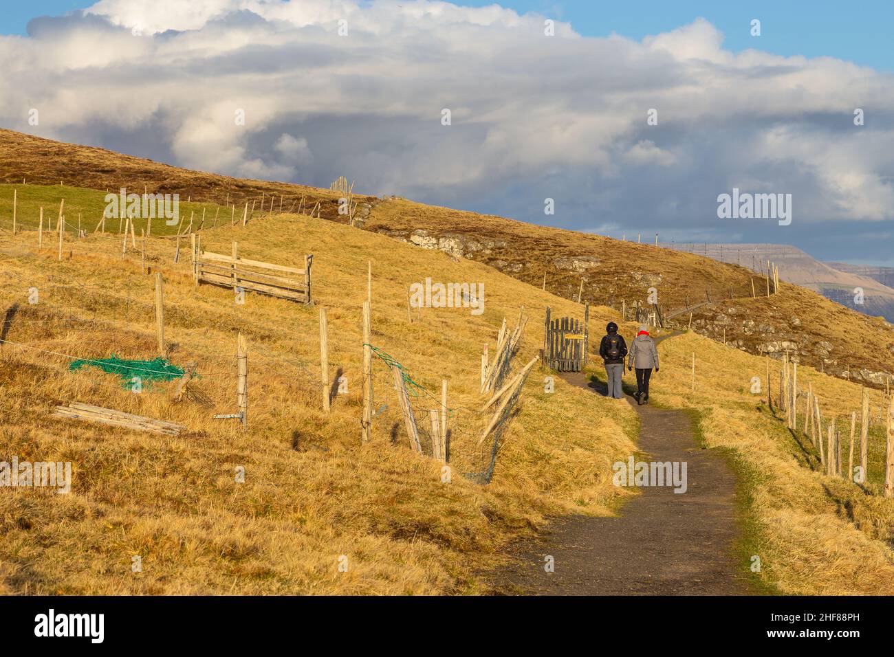 Sandavagur, Faroe Islands - 28 April 2018: Tourists on the path of a Witch Finger. Hills around. Sunny spring evening. Stock Photo
