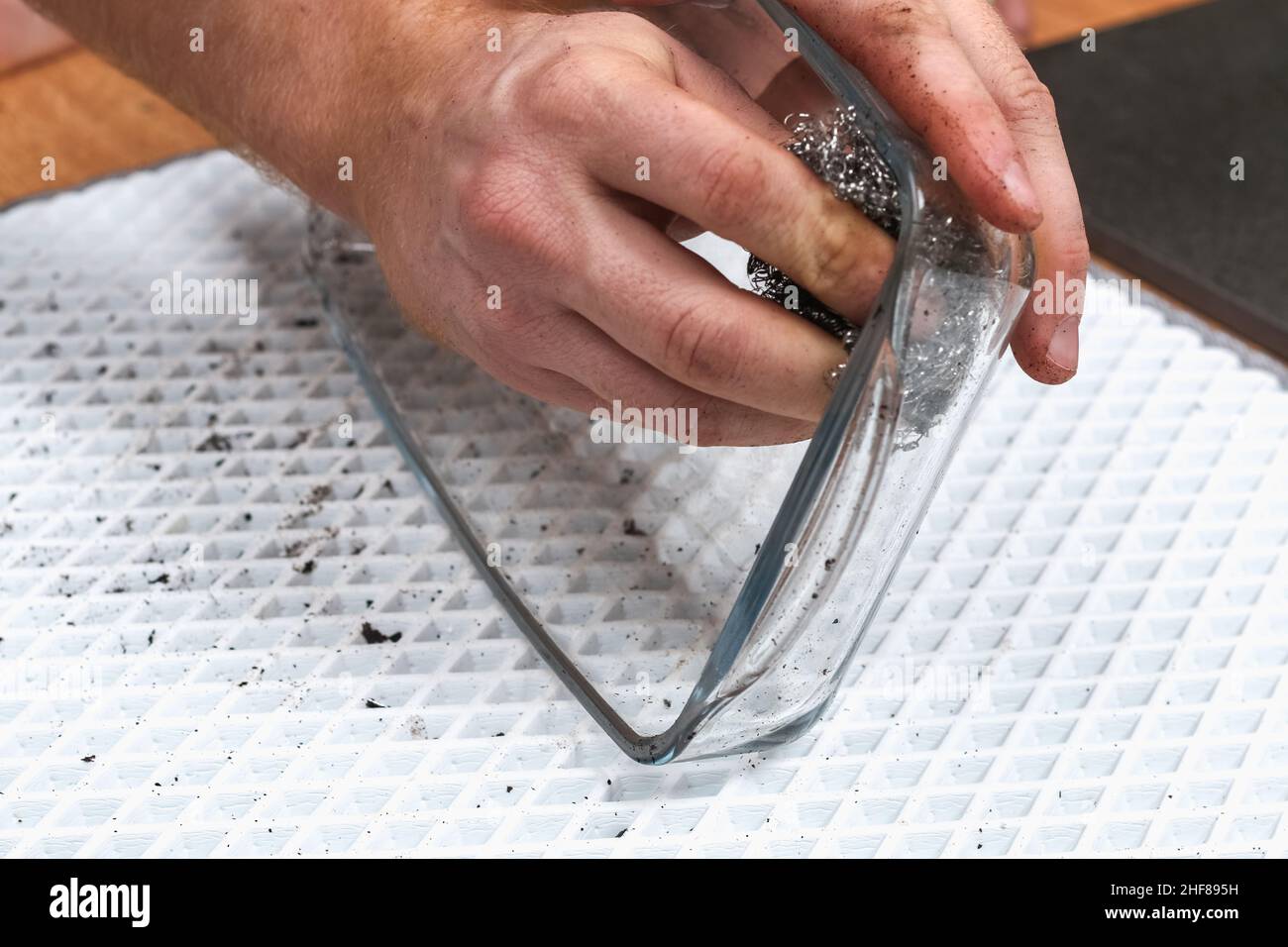 A man is cleaning a dirty baking dish with a thick layer of carbon with